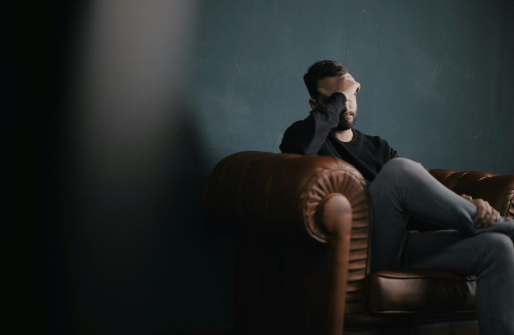 A man sitting on a chair with his hand on his forehead, representing disability considerations for depression.