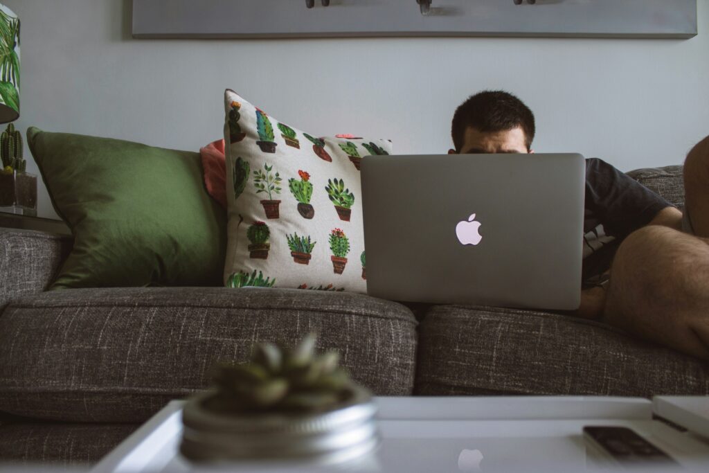 A man sitting on a couch using a laptop, learning about SSDI and other benefits he may qualify for.