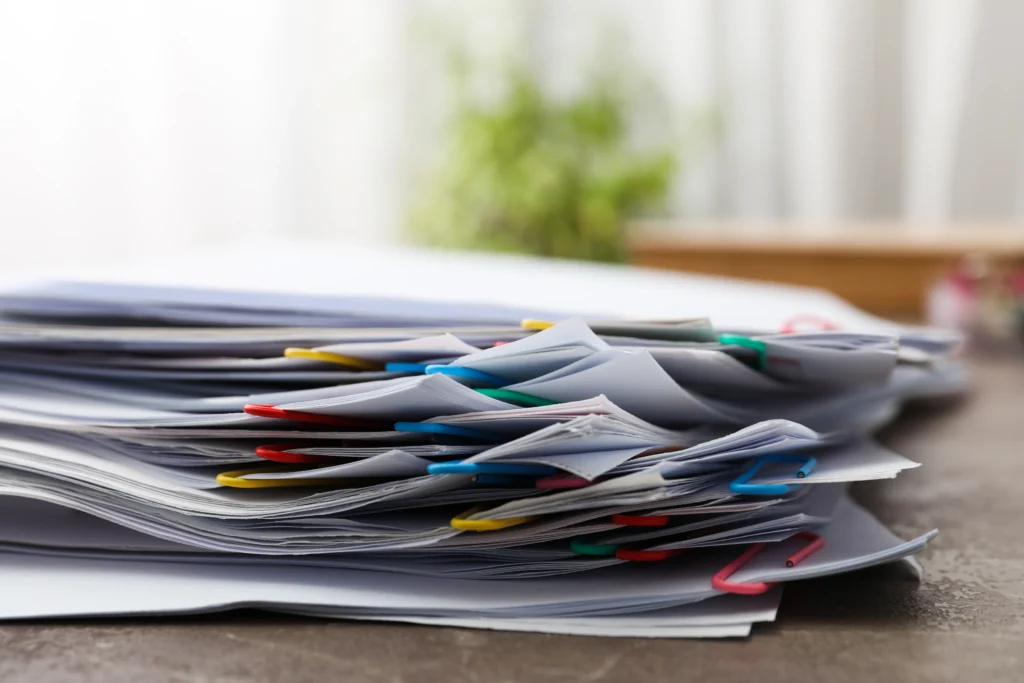 A stack of neatly organized documents with colorful paper clips on a table, symbolizing thorough preparation for an SSA hearing. These documents, critical for a disability claim, include medical records, employment history, and personal testimonies, essential for presenting a strong case.