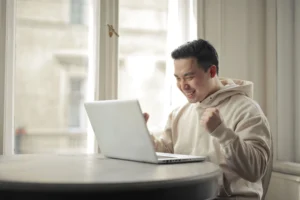A man wearing a hoodie is seated at a table, engaged with his laptop, reflecting on the importance of a local SSDI attorney.