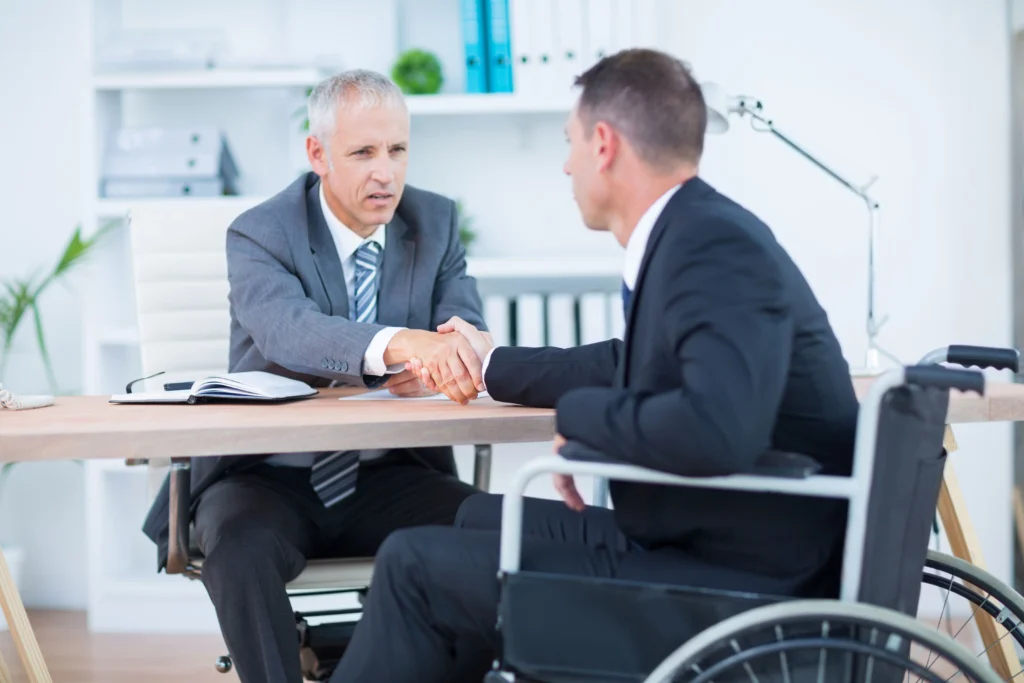 Disability lawyer shaking hands with a client in a wheelchair after discussing short-term and long-term disability benefits